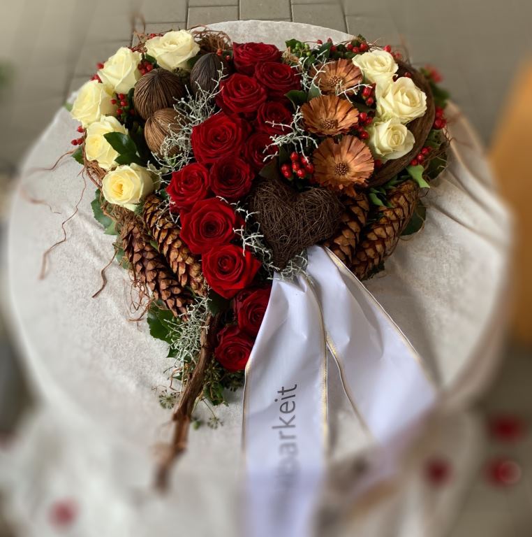 Gesteck aus roten und weißen Rosen mit Zapfen und Schleife