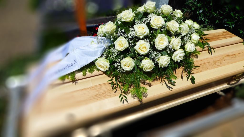 Sargbukett aus weißen Rosen auf einem hellen Holzsarg