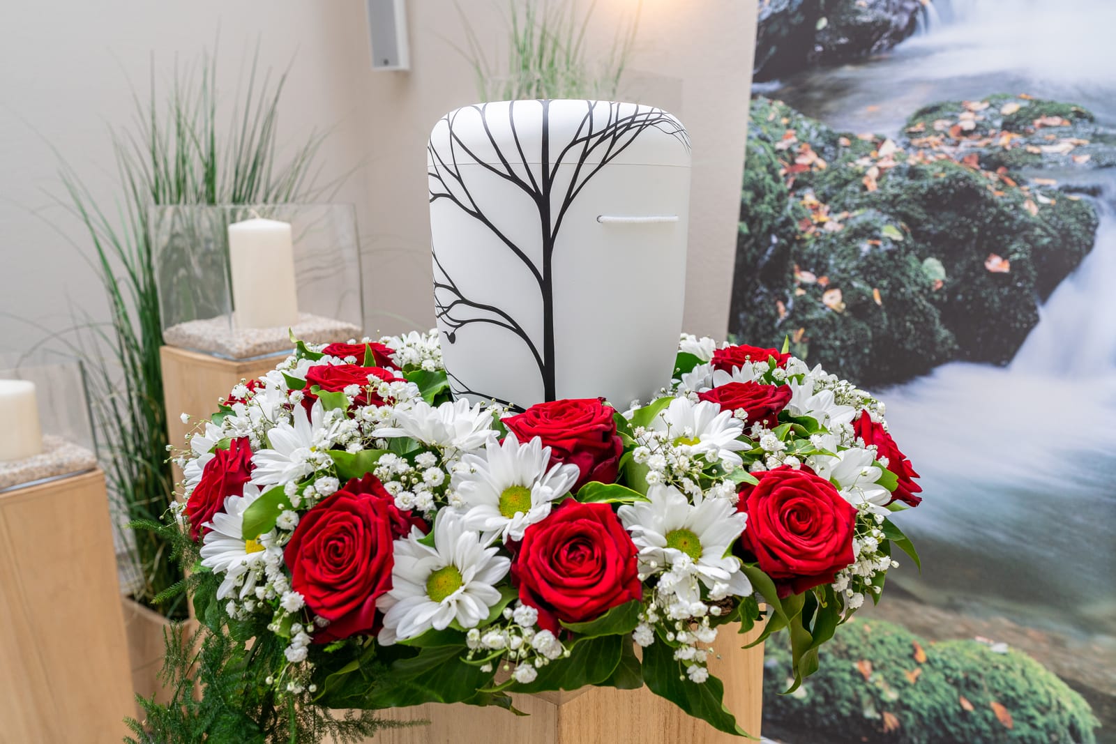 Urne mit Baummotiv, umgeben von einem Kranz aus roten Rosen und weißen Margeriten